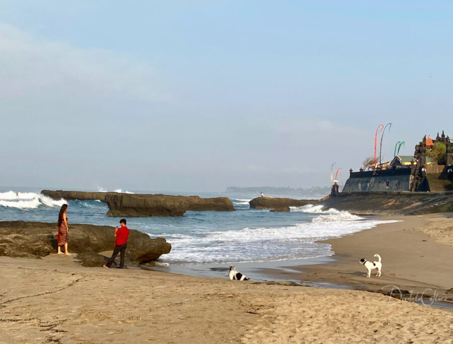 Tempel am Strand von Canggu im Süden Balis, Bunte Wimpel ragen in den Himmel, Surfer genießen die hohen Wellen, die an den Strand rollen