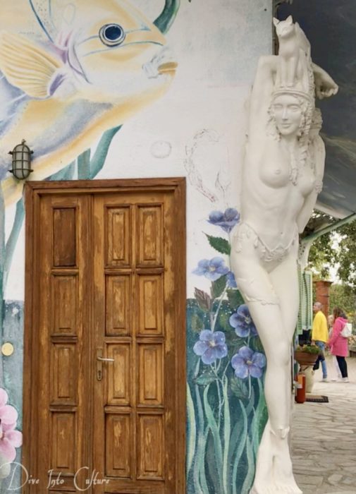 Gemeinschaft Damjl, Kunstfertigkeit an Wohnhaus, mit Wandmalerei und über 2 meter großer, weißer weiblicher Tonfigur an Hausecke